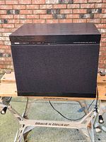 Front view of Yamaha NS-W2 powered subwoofer showing black wood grain finish, speaker grille, and control panel.