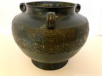 Front side view of antique bronze champleve pot showing overall shape, three loop handles, and etched enamel band.