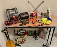 Overall lot showing battery chargers, jumper cables, tow straps, automotive fluids, tire iron, ice scraper, shovel, and garage mirror.