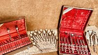 Two velvet-lined boxes displaying the full flatware collection which includes forks, spoons, knives, ladles, and serving utensils in a gold-tinted bamboo motif design.