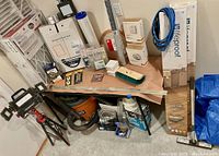 Full lot showing many items including packages of Lifeproof flooring, air filters, hardware and shopvac under table.