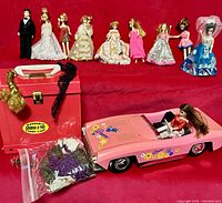 Photo showing eight Dawn dolls in a row dressed in different outfits and a pink toy Corvette car with a doll inside, red carrying case, and bag of accessories.