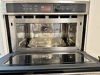 Open microwave oven showing stainless steel interior and glass turntable.