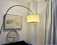 Full view of corner with curved brass finish floor lamp, white fabric shade, gold metallic Massachusetts map wall art on linen canvas, and geometric accent orb on table.