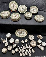 Full set of plates, bowls, cups, spoons, ladles, and cruets displayed on black cloth background, showing detailed hand-painted designs with gold accents.