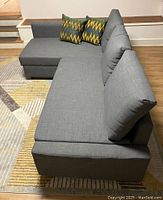 Photo of entire gray L-shaped sleeper sofa from a side angle showing chaise on the left, colorful pillows, and removable back cushions.