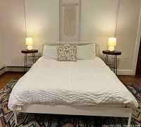 Full view of queen bed with bedding including pillows and accent pillow, two bedside tables with lamps