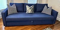 Frontal view of royal blue sleeper sofa with three throw pillows on hardwood floor.