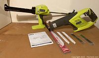 Photo showing Ryobi reciprocating saw and caulking gun with several saw blades laid out, plus instruction manual on cardboard surface.