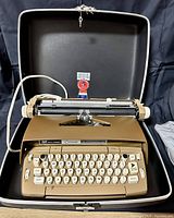 Front view of tan Smith Corona Coronet Automatic 12 electric typewriter inside black hard-shell carrying case with open lid.