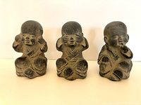 Front view of three vintage ceramic figurines with rubbed blackened finish representing hear no evil, see no evil, speak no evil in a seated pose.