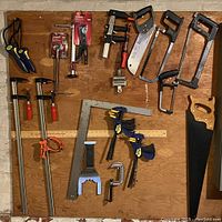 Overview photo showing various clamps, saws, squares, and pipe wrench arranged on wall