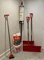 Full set of the snow removal tools including roof rake, ice chopper, two red snow shovels, and ice melt bags in bucket and bag.