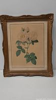 Full view of painting showing white floral artwork within ornate carved wooden frame against a neutral background.