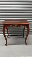 Front view of the antique wooden side table showing tabletop and curved legs with brass ornamental details.