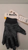 Photo of Bench Active Gloves showing front side with black and grey camo pattern and knit cuff with retail tag attached.