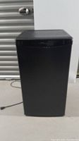 Full view of black Danby Designer mini fridge from front with door closed, showing compact rectangular shape and power cord.