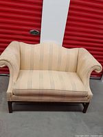Loveseat couch front view showing beige upholstery with vertical stripes, curved backrest, and rolled arms with wooden legs.