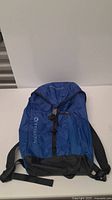 Front view of blue Merrell sports backpack showing logo, front zipper pocket, black buckle and straps