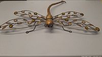 Metal dragonfly sculpture from top front angle, showing detailed wings with circular gold-colored accents, body, and legs.