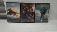 Front view of three Yellowstone DVD cases for Seasons 1, 2, and 3 placed side-by-side on a white surface.