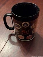 Front side of the black NHL Thermos mug showing multiple 1970s NHL team logos including Toronto Maple Leafs, Montreal Canadiens, NHL shield, and others.