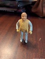 Front angle close-up of Boss Hogg action figure on a dark wood surface, showing facial details and outfit.