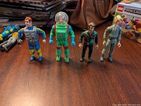 Front view of the four Ghostbusters action figures standing upright side by side on a wooden surface with other items in the background.
