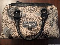 Front view of satchel showing floral and leopard pattern with GUESS logo plate and black leather handles.