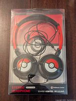 Front view of the headphones inside sealed packaging showing the Pokeball designs on each earcup and red headband.