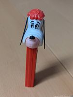 Front view of the PEZ Droopy Dog dispenser showing the head with red hair, white face, black eyes and nose, and orange base.