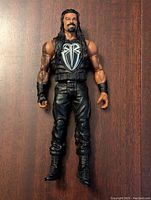 Front view of Roman Reigns wrestling figure standing on a wood surface, showing detailed outfit and facial likeness.