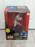 Front view of the Obi-Wan Kenobi figure bank in the original box showing figure in combat pose with lightsaber inside packaging.