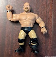Front view of the Steve Austin WWE action figure showing muscular build, black trunks, and left arm raised.