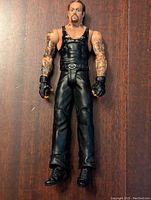 Front view of The Undertaker WWE action figure showing detailed tattoos, black attire and facial features.