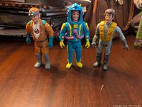 Front view of three Ghostbusters figures arranged side by side on wooden surface