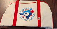 Front side of the bag with Toronto Blue Jays logo and red straps on a white canvas background.