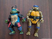 Two TMNT 1980s Playmates action figures: Donatello and Leonardo side by side on a wood floor