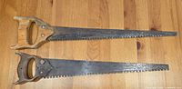 Two antique/vintage double blade handsaws laid flat showing wooden handles and metal blades with dual edges.
