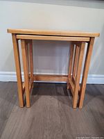 Side view of two nested wooden tables showing rectangular legs and clean design.