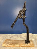 Side view of the antique bottle capper mounted on a wooden base showing lever handle and top screwing part.