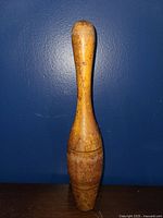 Single wooden bowling pin standing against a dark blue wall, clear view of size and shape.