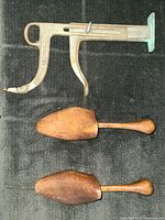 Photo shows two wood shoe stretchers with wooden handles and natural finish alongside a metal shoe measuring device with embossed 'McCOOLTER & SON'. Items laid on a black fabric.