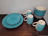 Photo showing three tall blue ceramic cups with handles, five blue and white bowls stacked, and one large and one small blue plate laid flat