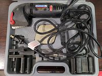 Photo of a black Dremel contour sander with variable speed, power cord, several sanding attachments, all stored in a fitted plastic carrying case.