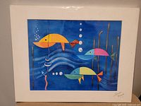 Photo showing colorful signed fish art painting with blue background and geometric styled fish, signed by the artist.