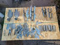 Several galvanized steel hangers and structural connectors arranged on plywood surface outdoors.