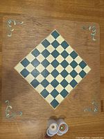 Top-down photo of homemade chess board showing 8x8 checkered playing area with natural and black squares, mounted on square wooden frame with metal corner decorations. Measuring 14 inches on each side.