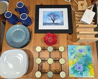 Photo of the full lot including blue mugs, blue plates, white plates, candle holders, wooden charging station, and framed art.