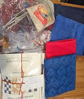 Top view of assorted knitting needles, yarn packages, blue and red fabric pieces, and quilting patterns tied together with string